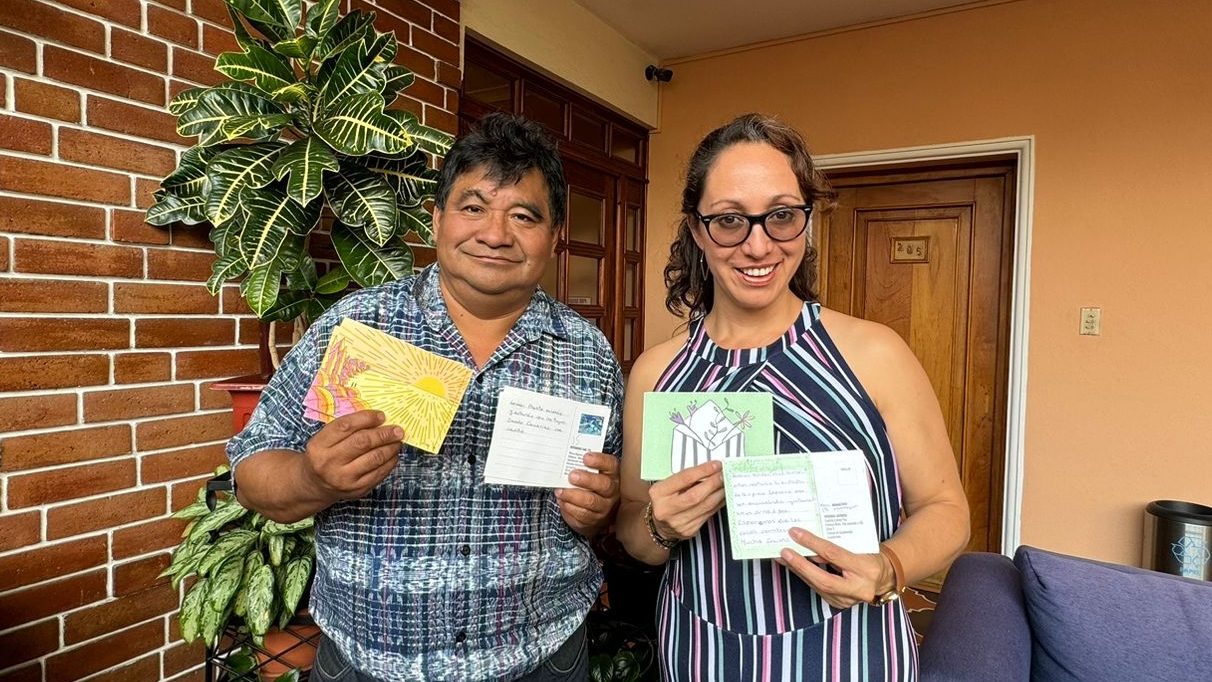 Virginia Laparra and Bernardo Caal Xol stand together holding postcards of solidarity.